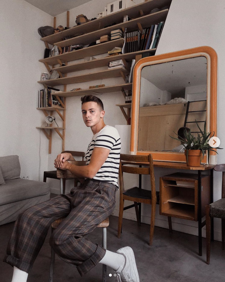 guy sitting on a stool in front of a desk with a mirror and a wall of shelves