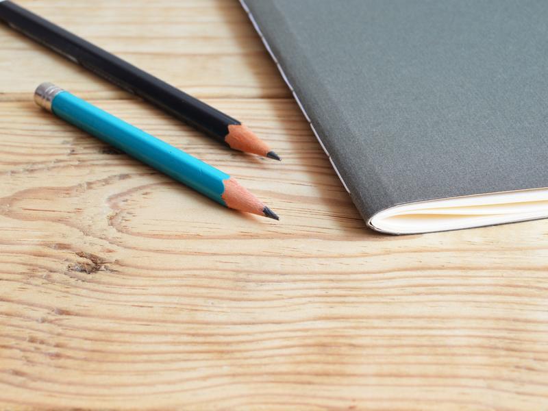 2 pencils and a notebook lying on a wooden desk